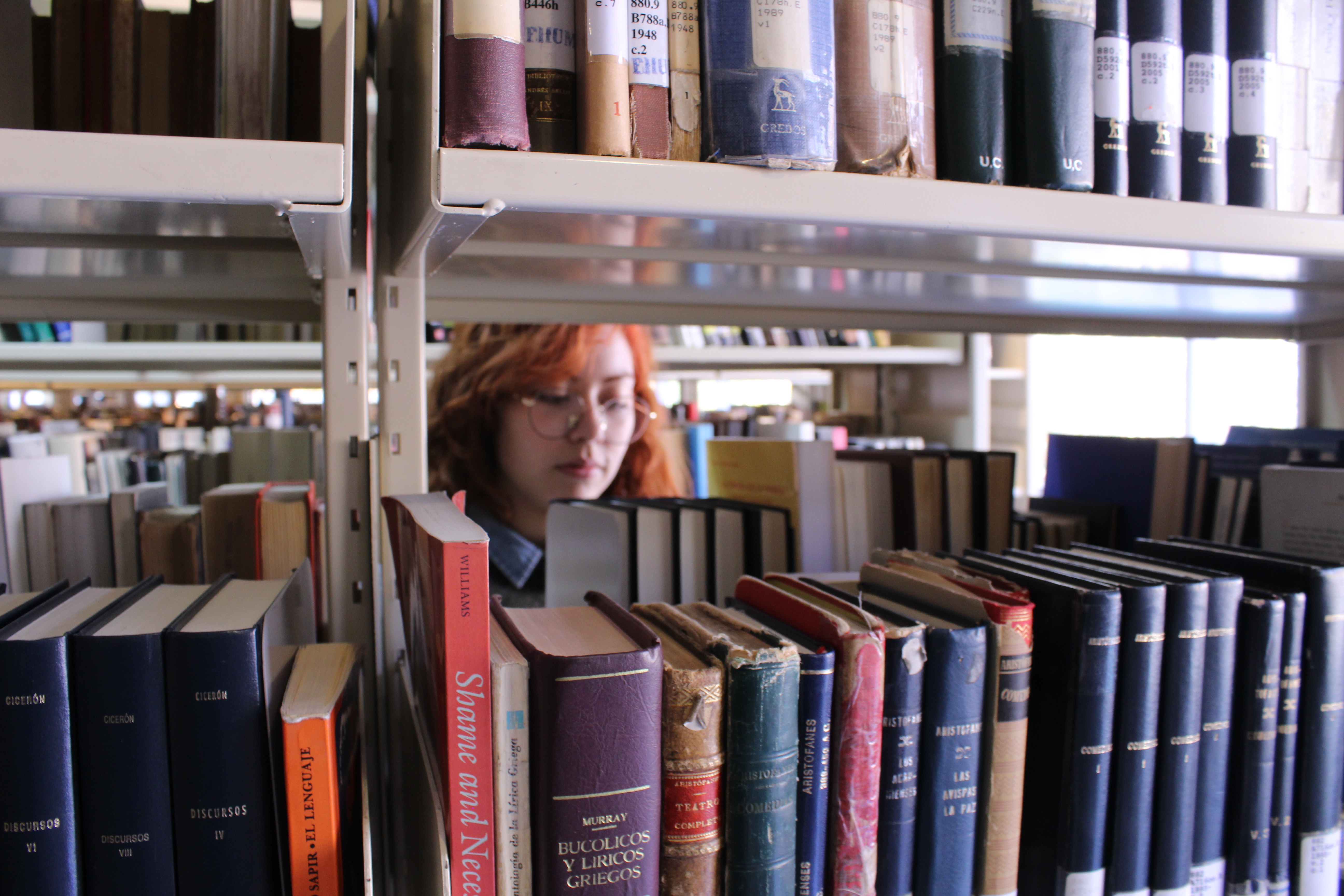 Fotografía de una estudiante entre una estantería de libros. 