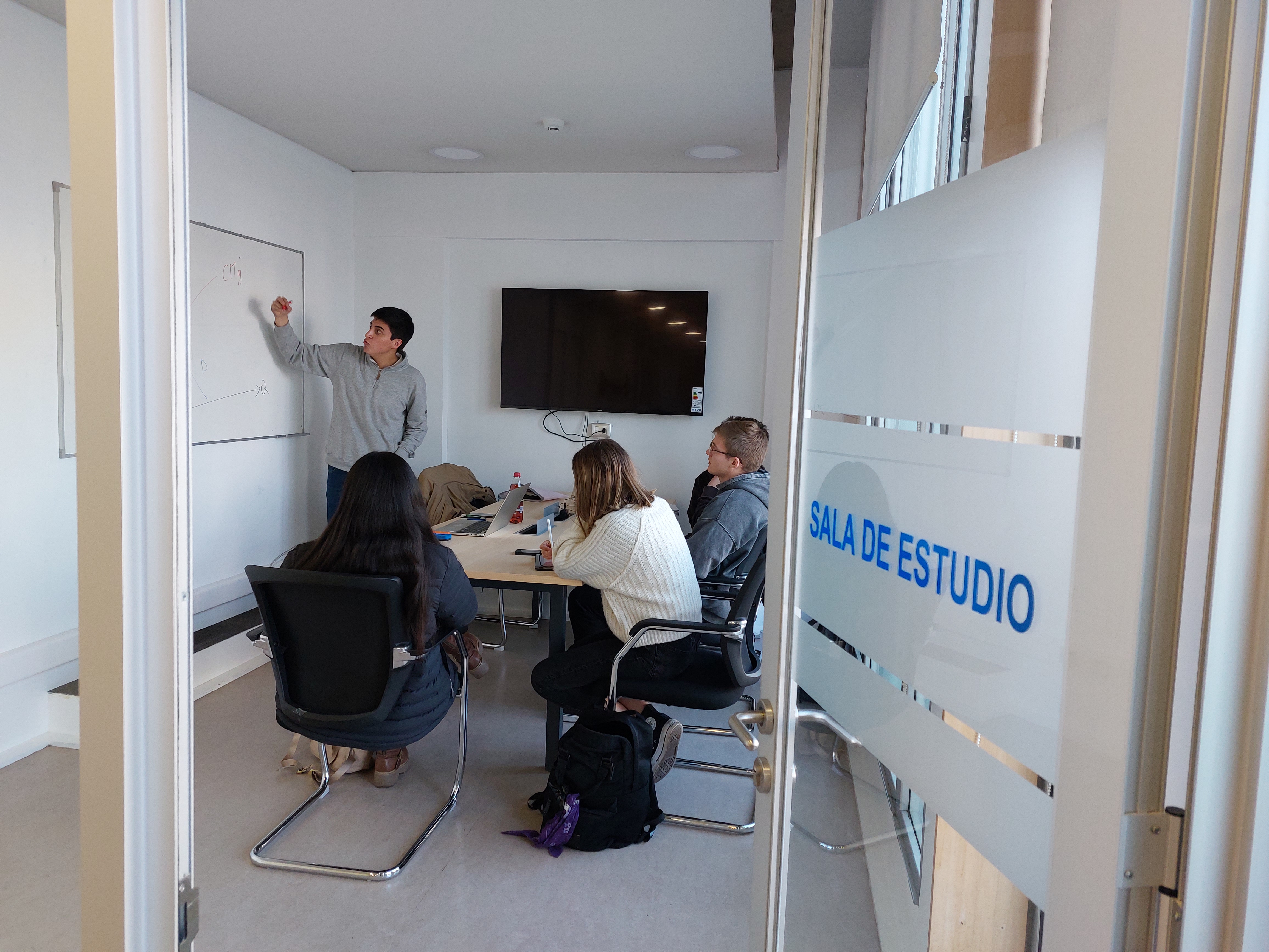 Fotografía de la sala de estudio en Biblioteca de Teología siendo ocupada por tres personas que conversan y usan la pizarra.