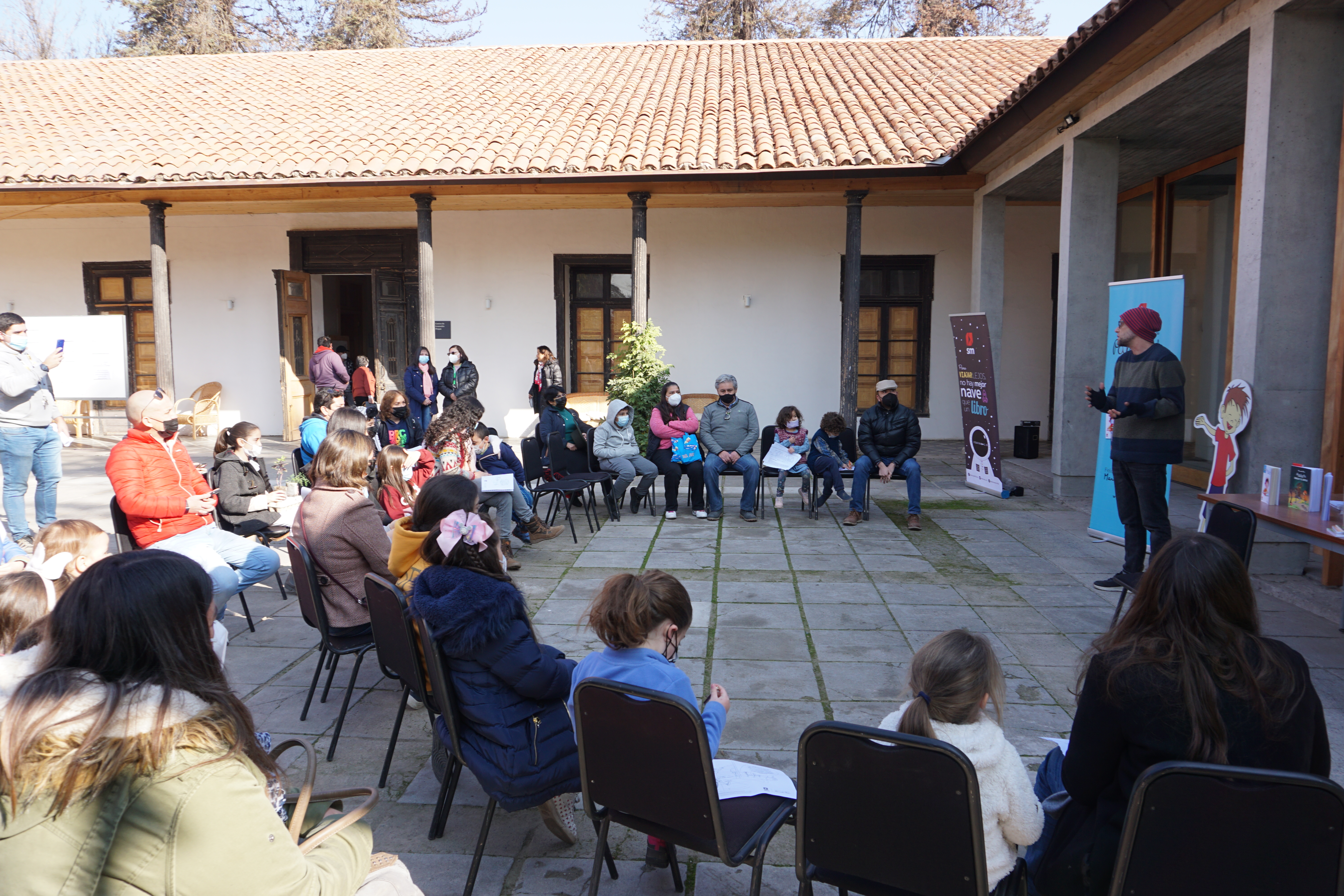 Fotografía de actividad realizada en la Biblioteca Escolar de Pirque en años anteriores. Se ve un círculo de personas escuchando y mirando a una persona que cuenta o explica algo.
