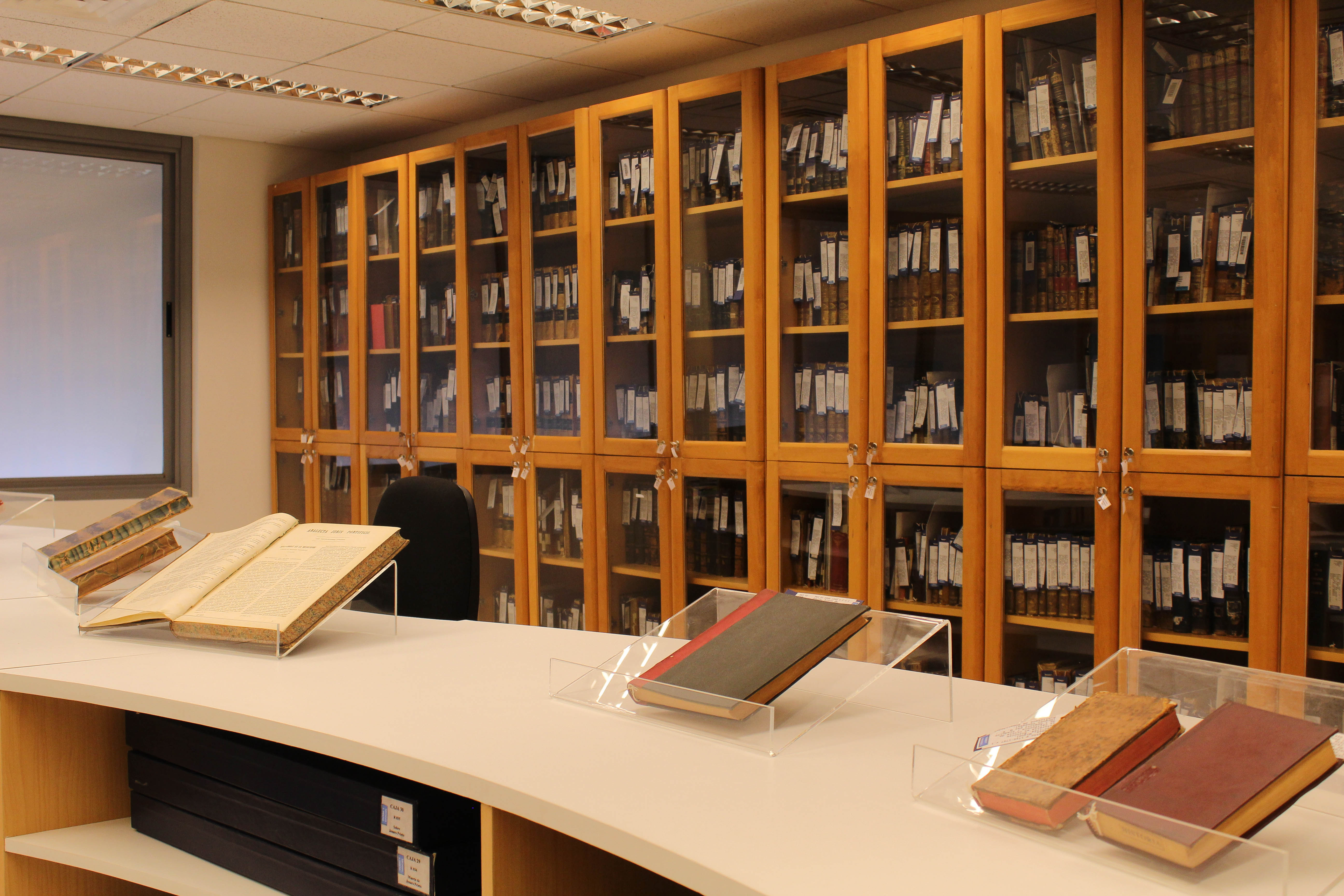 Fotografía de la sala patrimonial de Biblioteca de Humanidades. Se ve una estantería de vidrio en el fondo y algunos libros en exhibición sobre una mesa. 