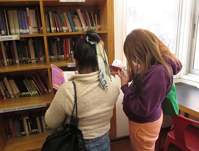 Fotografía de dos estudiantes del Centro Penitenciario Femenino revisando libros de una estantería.