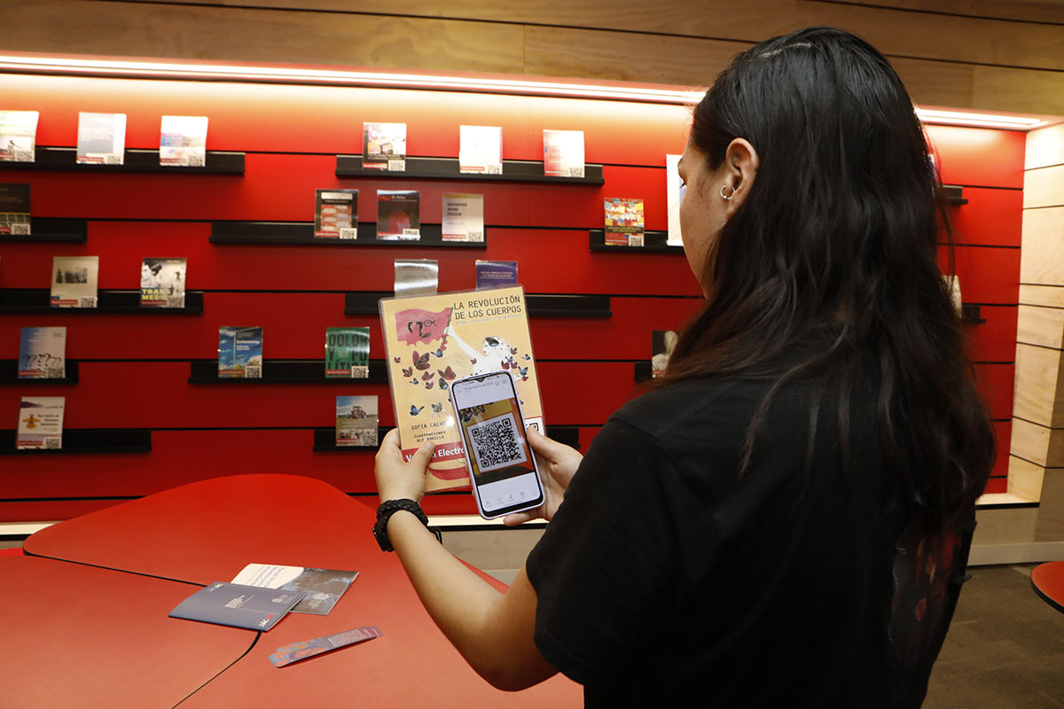 fotografía de una estudiante escaneando un código QR para acceder a un recurso electrónico de la colección de género de biblioteca san joaquín.